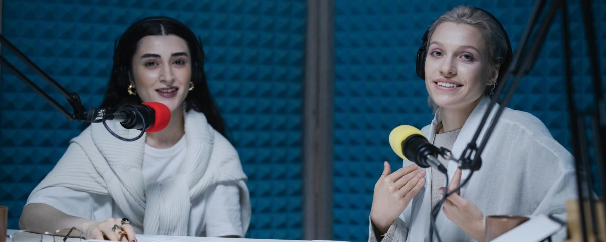 Two women podcasters engaging in discussion inside a modern recording studio with microphones.